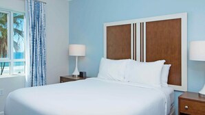 A hotel room with a large bed, two bedside tables, a nightstand, and a view of the ocean through the window. - Oceanfront 2BR Deluxe at Club Wyndham Oceanside Pier Resort in California (Oceanside)