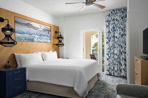 A hotel room with a bed, two wall-mounted lamps, a ceiling fan, a painting, a TV, and a patterned curtain.