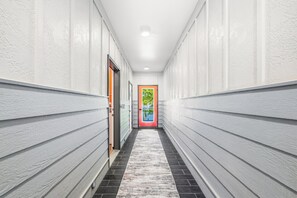 Ein Flur mit weißen Wänden, einem schwarz-weißen Fußboden und einer Tür mit einem farbenfrohen Fenster am Ende.