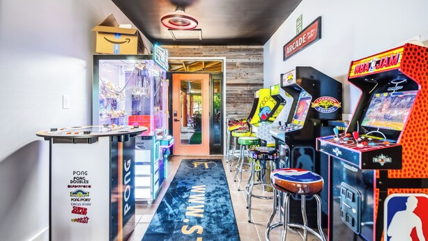 Un pasillo con juegos de arcade, una mesa de ping pong y una puerta que da a una habitación.