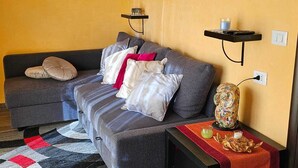 A living room with a sofa, pillows, a small table with a vase and snacks, and a wall-mounted shelf. - Luxury Suite (Palmi)