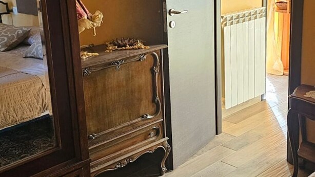 A room with a bed, a wooden wardrobe, a door leading to another room, and a patterned rug. - Luxury Suite (Palmi)