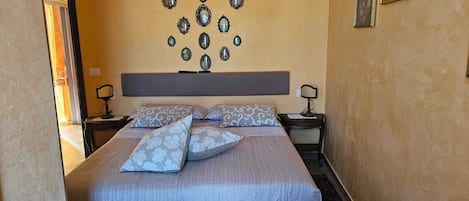 A bed with patterned bedding, a headboard, bedside lamps, and wall-mounted mirrors.
