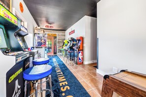 A gaming arcade with various machines, a blue carpet with text, and a wooden bench. - FUN TIMES LUXURY RESORT-3BD/2BA-LAKEFRONT-POOL-ARCADE-PLAYAREA-DOG AREA-MARINA (Jacksboro)