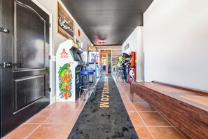 Un pasillo con juegos de arcade, una alfombra negra con el texto 'WELCOME' y un banco de madera.