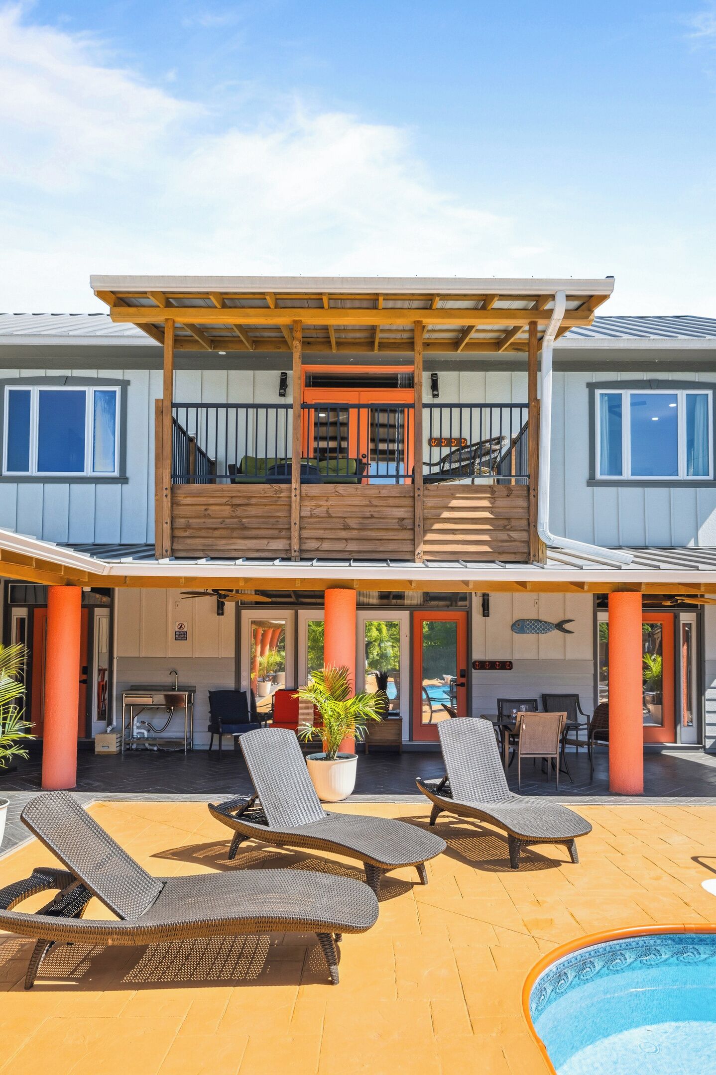 Ein zweistöckiges Haus mit überdachter Terrasse, Sitzgelegenheiten im Freien und einem Swimmingpool.