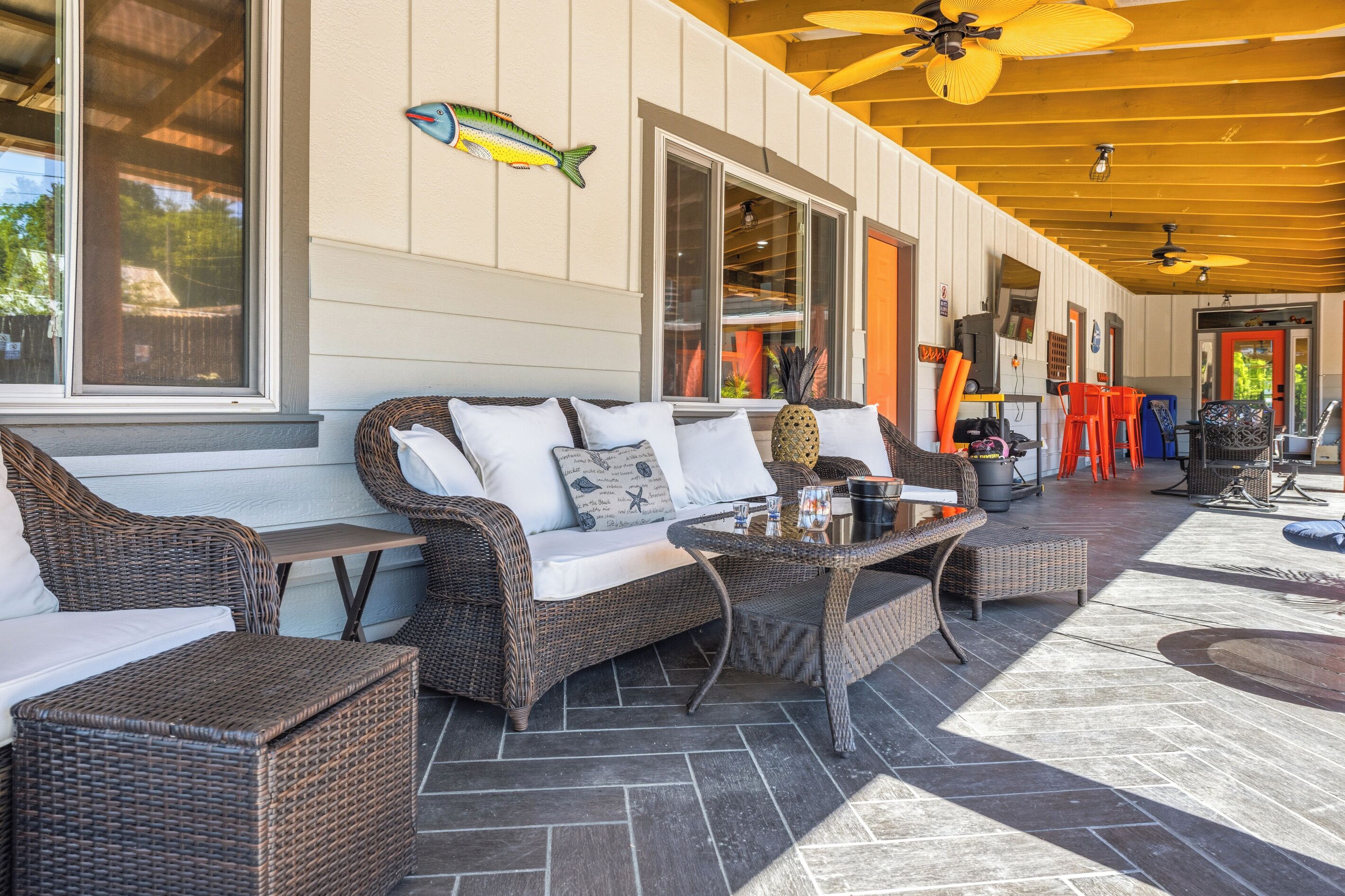 An outdoor patio with wicker furniture, a ceiling fan, and a fish decoration on the wall.
