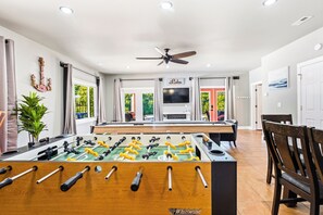 A room with a foosball table, a ceiling fan, and a TV mounted on the wall. - FUN TIMES LUXURY RESORT-2BD/1BA-LAKEFRONT-POOL-ARCADE-PLAYAREA-DOG AREA-MARINA (Jacksboro)