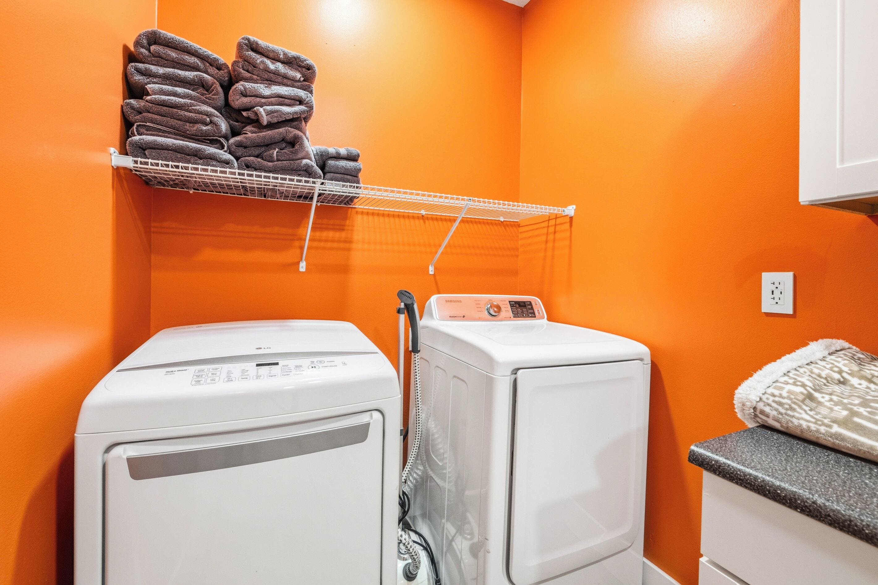 A laundry room with two washing machines, a drying rack with towels, and a power outlet on the wall.