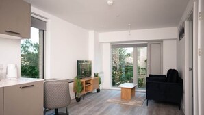 Un salon moderne avec un canapé, une table basse et un téléviseur. Une fenêtre offre une vue sur la verdure environnante.
