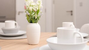 Une table à manger avec de l’assiette, des tasses et un vase à fleurs, le tout en céramique blanche.