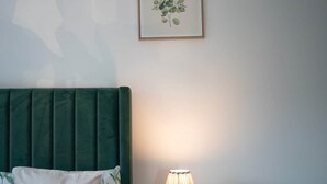 Une chambre avec deux lits, une table de chevet avec une lampe et une estampe botanique encadrée au mur.