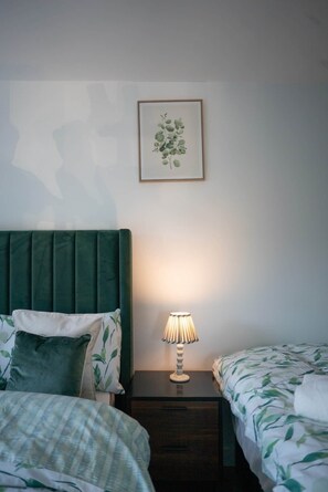 Ein Schlafzimmer mit zwei Betten, einem Nachttisch mit Lampe und einem gerahmten Pflanzenbild an der Wand.