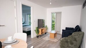 Habitació moderna amb taula de dinar, cadires, sofà, televisió i un llit al fons.