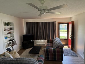 Ein Wohnzimmer mit Deckenventilator, Fernseher, Sofa, Couchtisch und einer zur Außenseite führenden Tür.