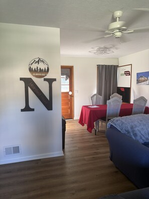 Ein Zimmer mit einem großen 'N' an der Wand, einem Deckenventilator, einem Esstisch mit Stühlen und einem Bett.
