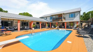 Ein zweistöckiges Gebäude mit Swimmingpool, Außenbereich zum Sitzen und einer überdachten Terrasse.