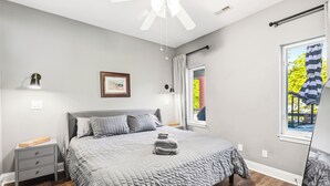 Ein Schlafzimmer mit Bett, Nachttischen, Deckenventilator, einem Fenster mit Vorhängen und einem gerahmten Bild an der Wand.