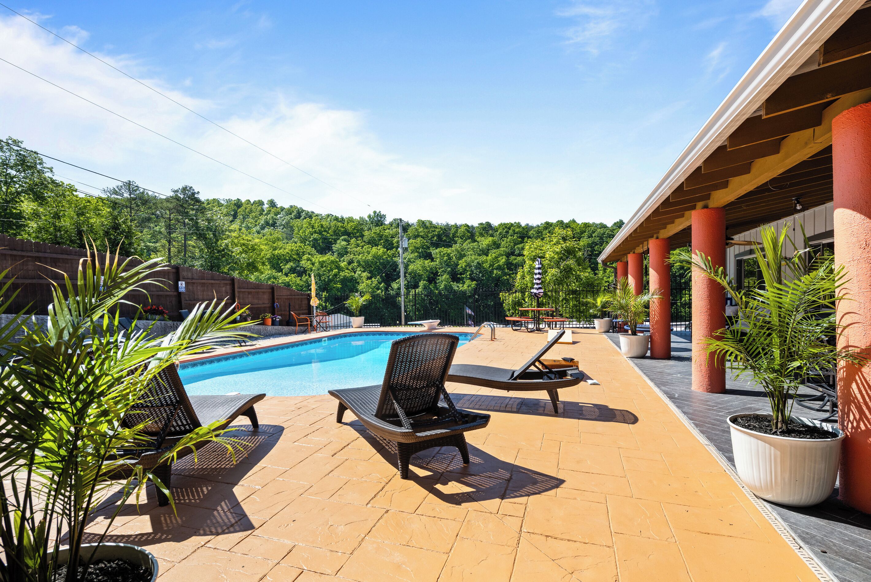 Ein Poolbereich mit Liegestühlen, einem Schwimmbecken und einer überdachten Terrasse mit Pflanzkübeln.