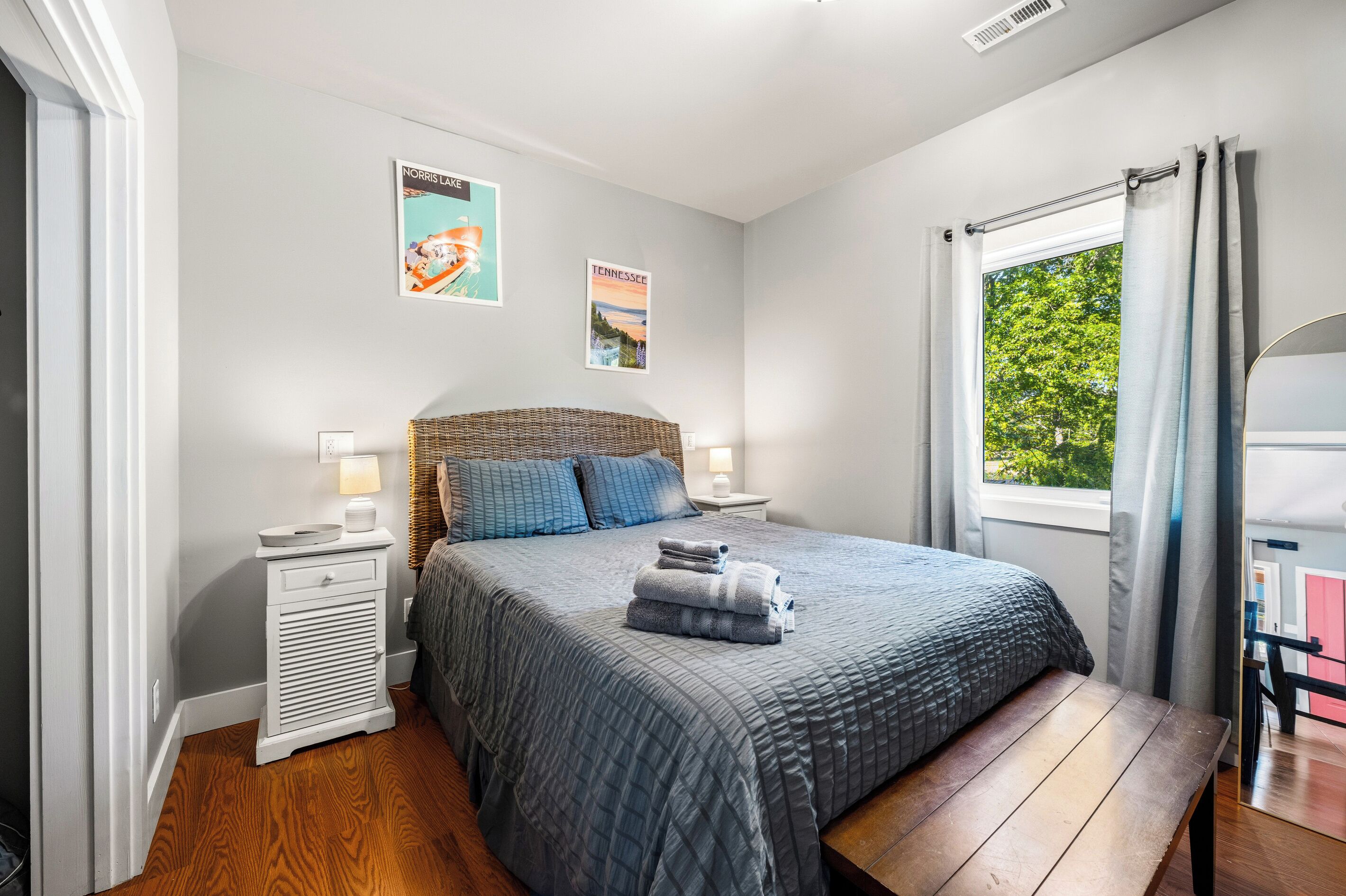 A bedroom with a bed, bedside tables, a window with curtains, and wall art.