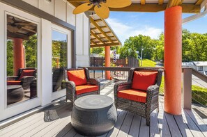 Een terras buiten met rieten meubels en een ronde tafel, een pergola met plafondventilator, en uitzicht op een groen landschap.