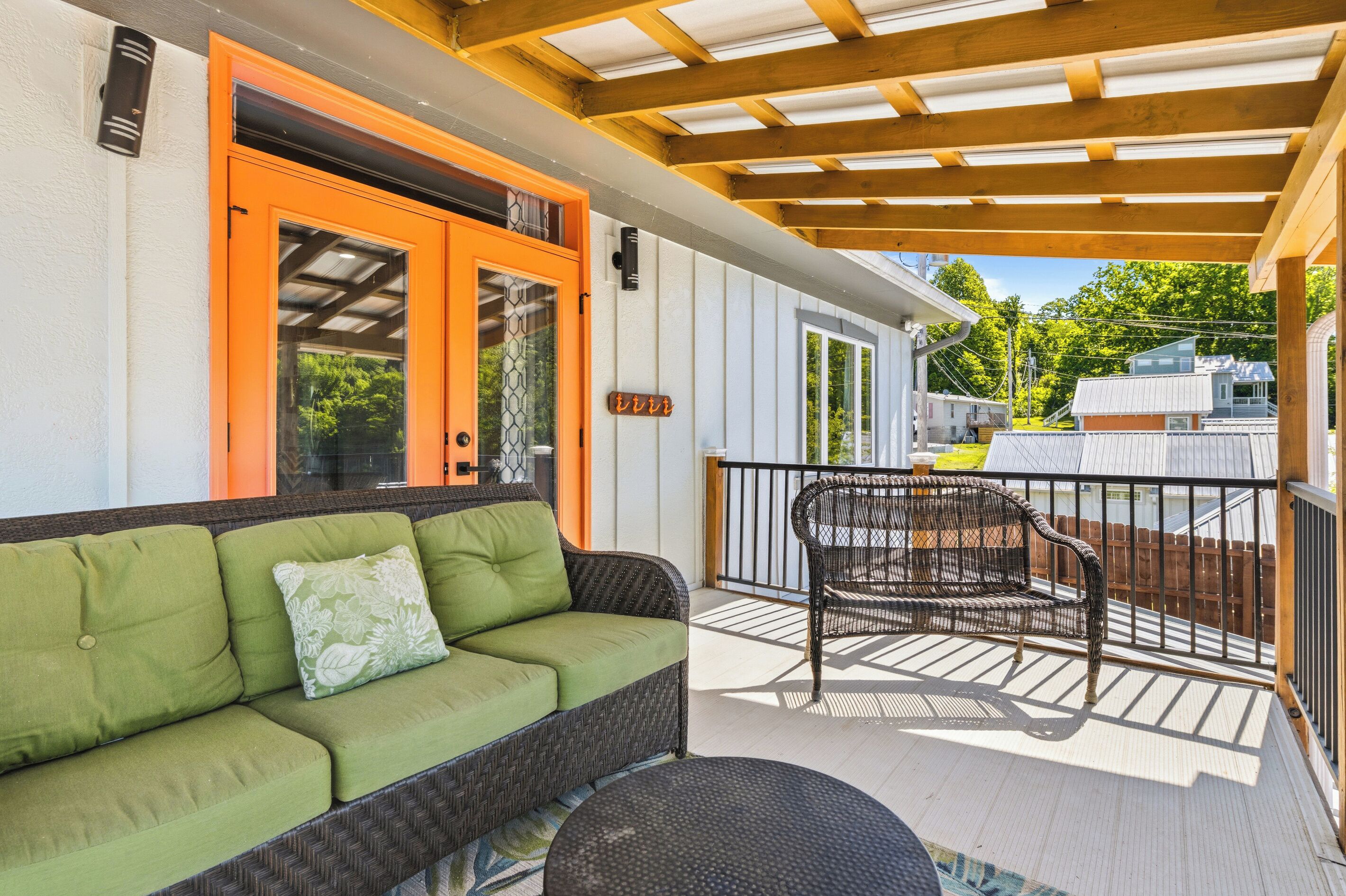 A covered outdoor area with a green sofa, a wicker chair, and a table with a drink.