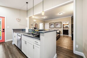 Een moderne keuken met een centraal eiland, hangende lampen en uitzicht op de eetruimte.