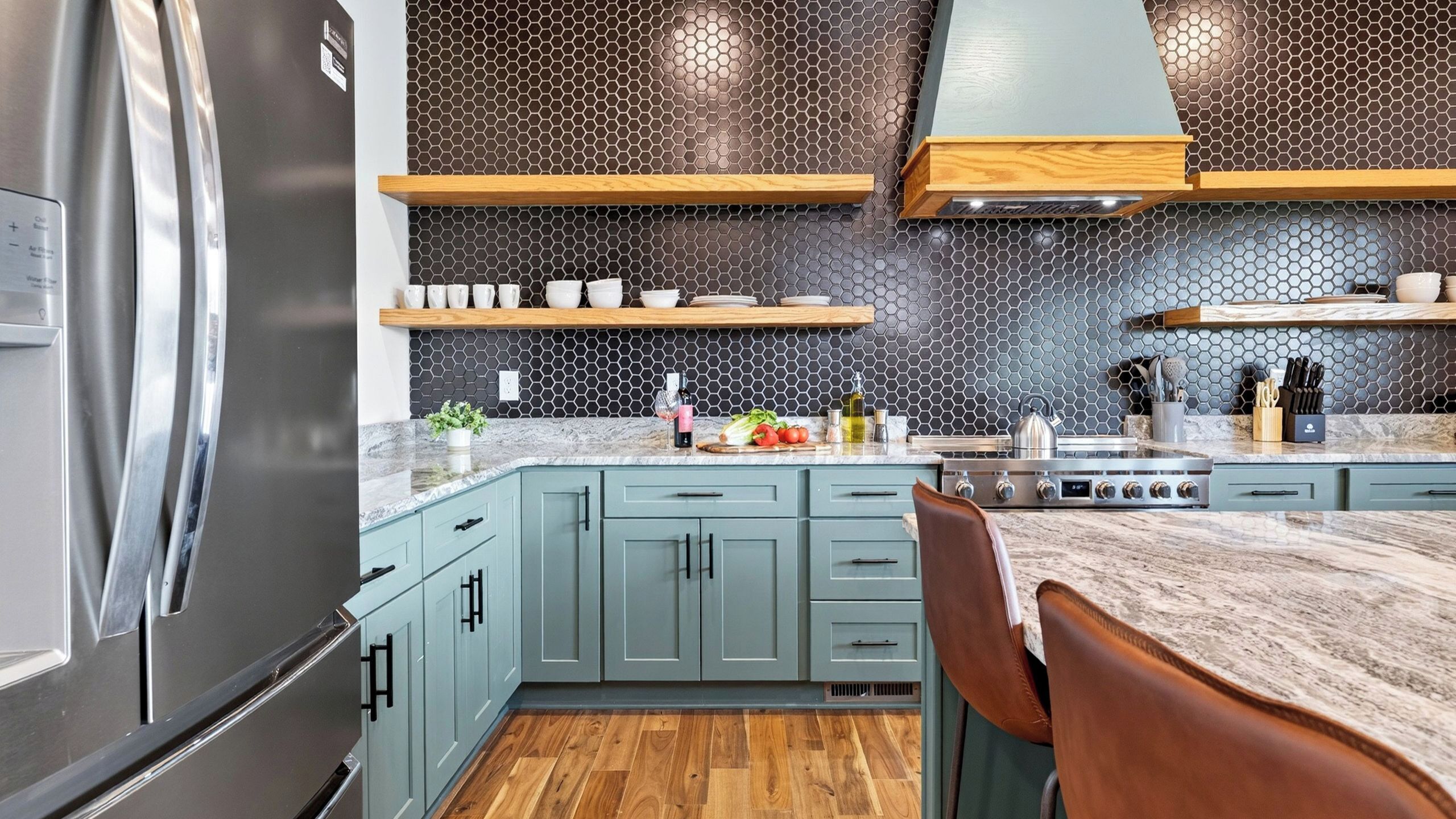 A modern kitchen with a stainless steel refrigerator, light blue cabinets, and a marble countertop.