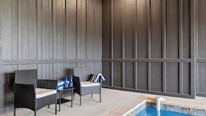 Ein Poolbereich mit zwei Korbstühlen und einem Tisch, einem gefliesten Pool und einer dunklen Holzverkleidung.