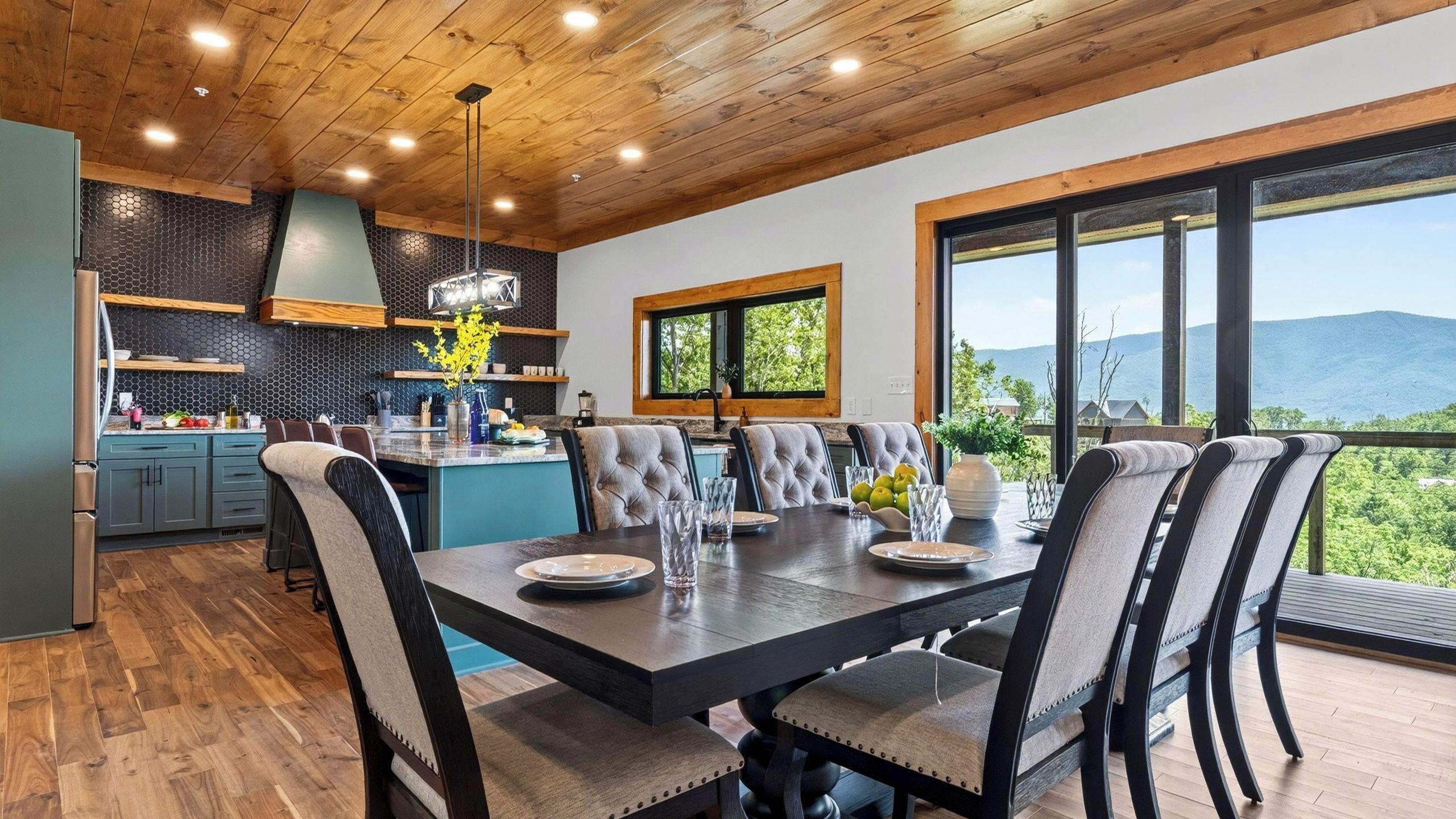 A modern kitchen with a dining area, large windows, and a view of the mountains.