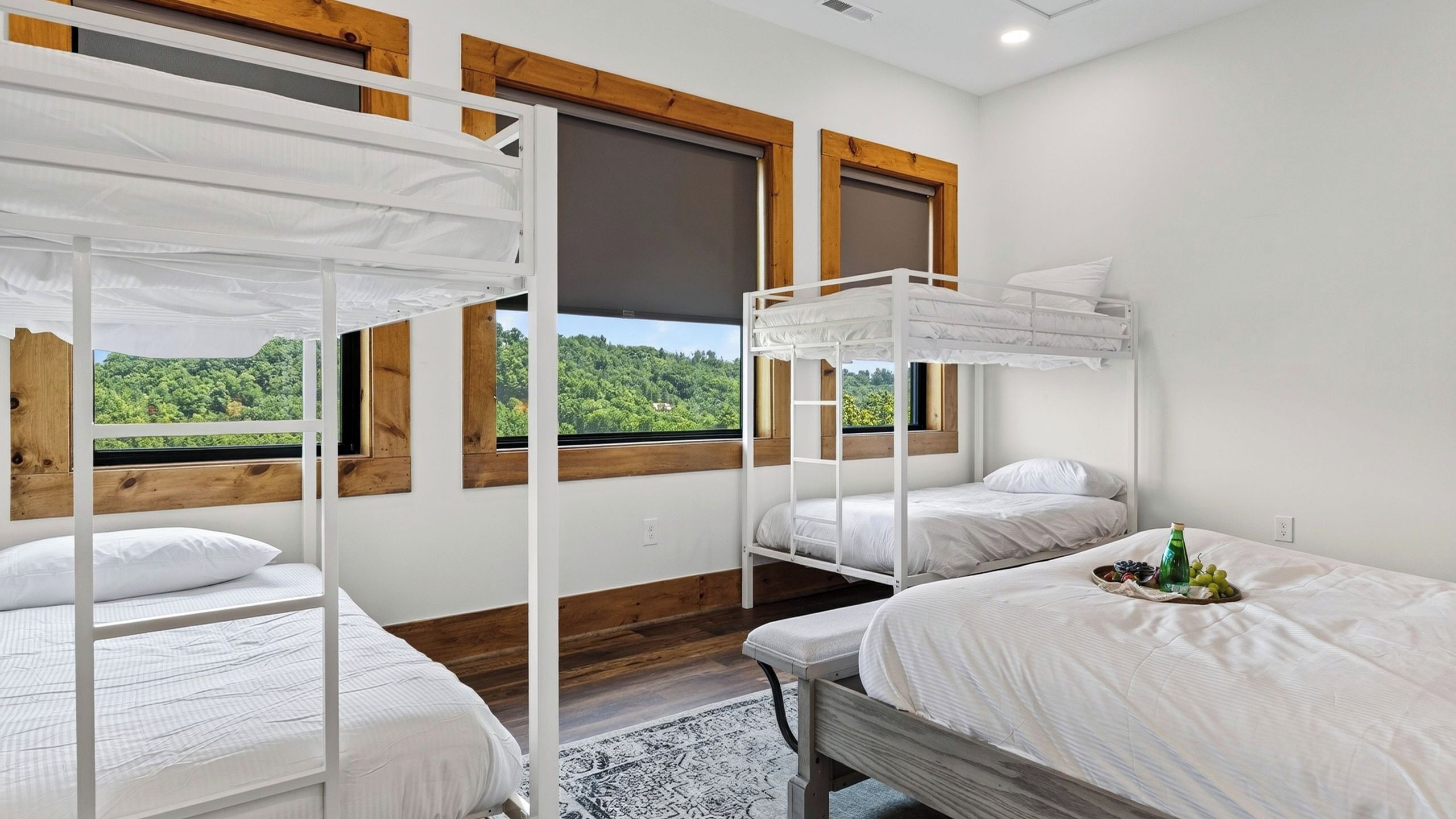 A room with bunk beds, wooden beams, large windows, and a view of greenery.