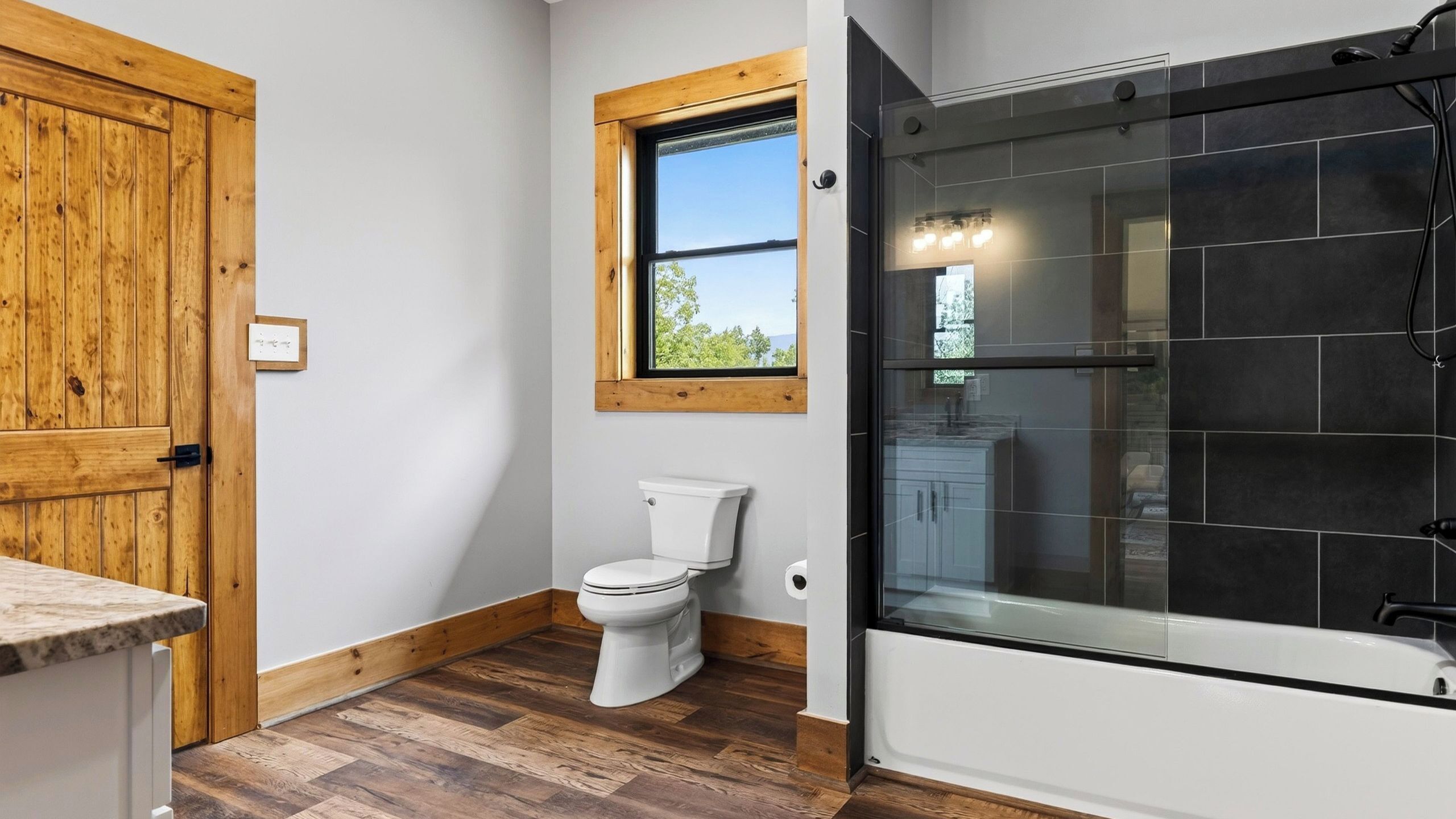 Un bagno con una porta in legno, un water, una finestra e uno spazio doccia con pareti in vetro.