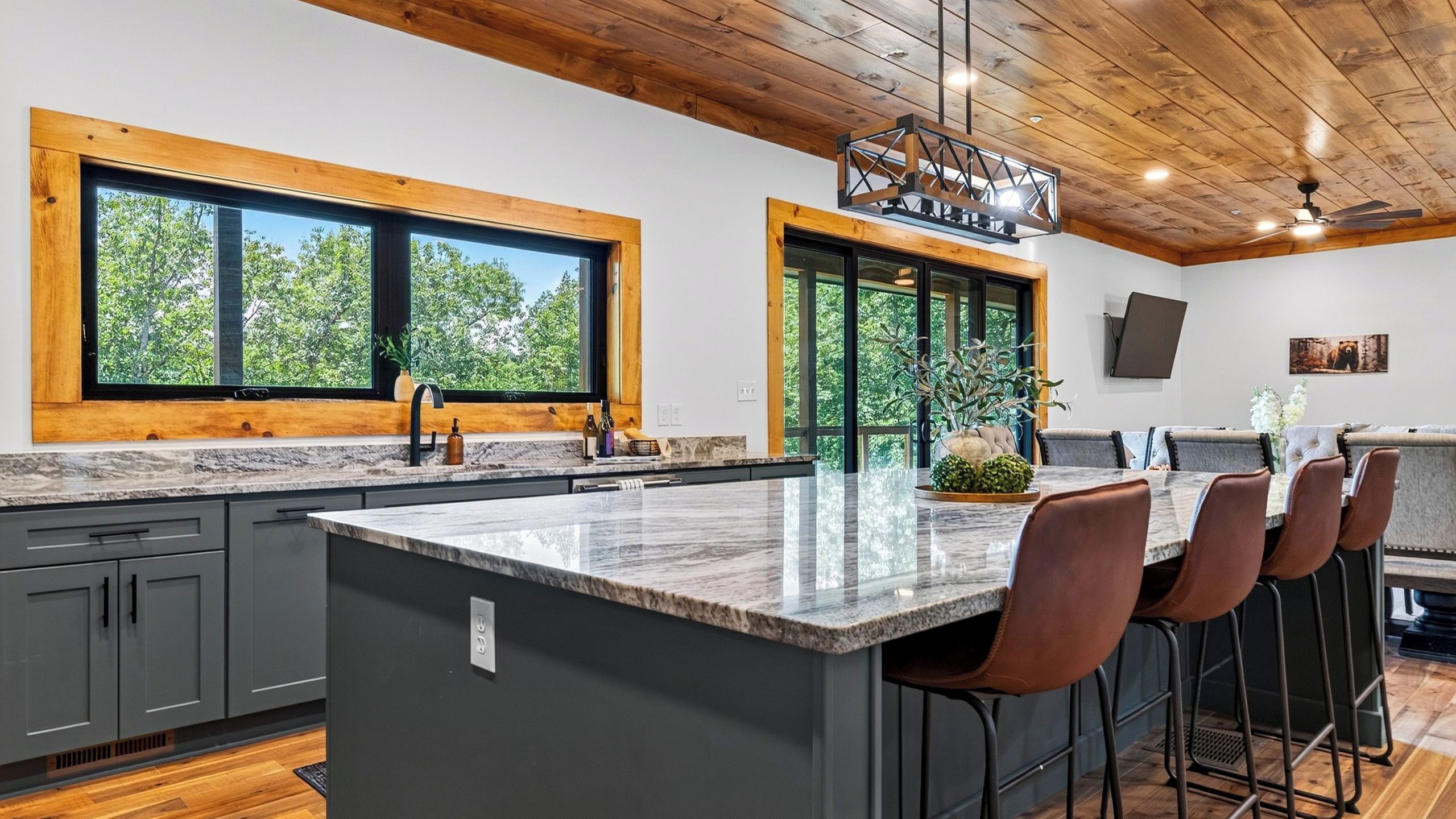 A modern kitchen with a large island, bar stools, and large windows with a view of trees.