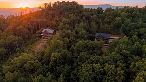 A forested area with two buildings, one with a balcony and another with a flat roof, surrounded by dense trees. - Spurling Retreat by Avantstay Sleeps 20 + Indoor Pool + Game Room Near Pigeon Forge (Sevierville)
