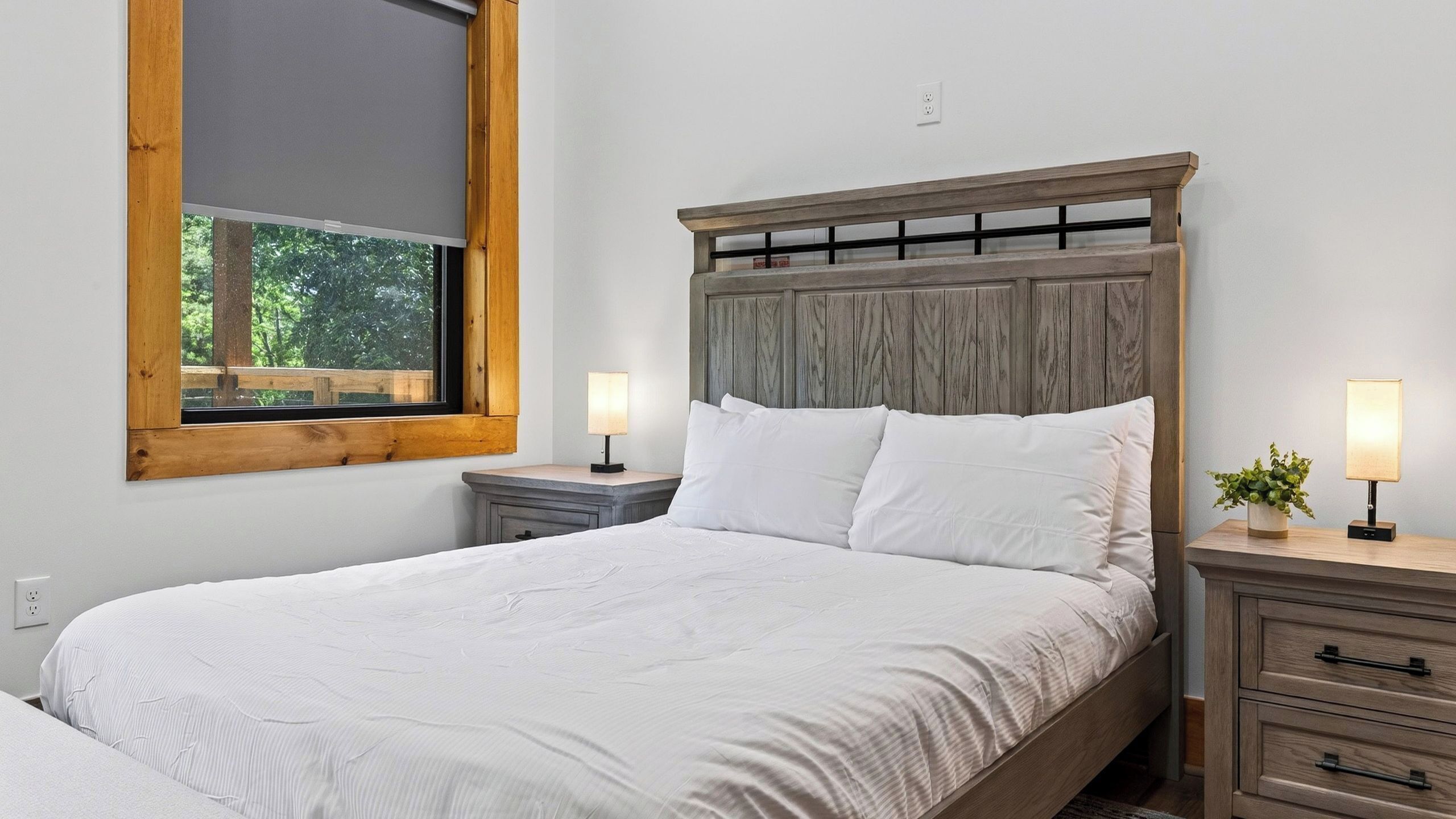 Une chambre à coucher avec une tête de lit en bois, une grande fenêtre, deux tables de chevet avec des lampes et un lit avec une literie blanche.