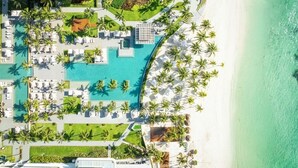 Vista aérea de um resort com piscina, palmeiras e uma praia.