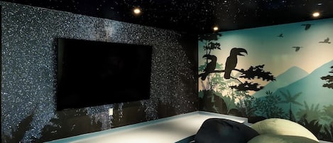 Ein Zimmer mit Sternenhimmel, einem an der Wand montierten Fernseher und einem Wandbild mit Vögeln und Pflanzen.