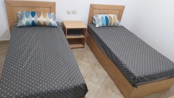 Two single beds with wooden headboards, a small wooden nightstand, and a tiled floor.