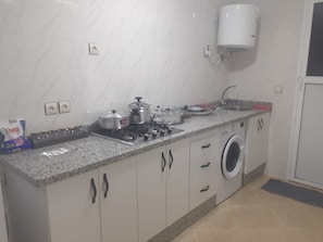 A kitchen with a gas stove, pots, a washing machine, and a microwave. - Immeuble Chaplin (Martil)
