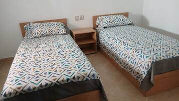Two single beds with geometric patterned bedding, wooden headboards, and a small wooden nightstand between them.