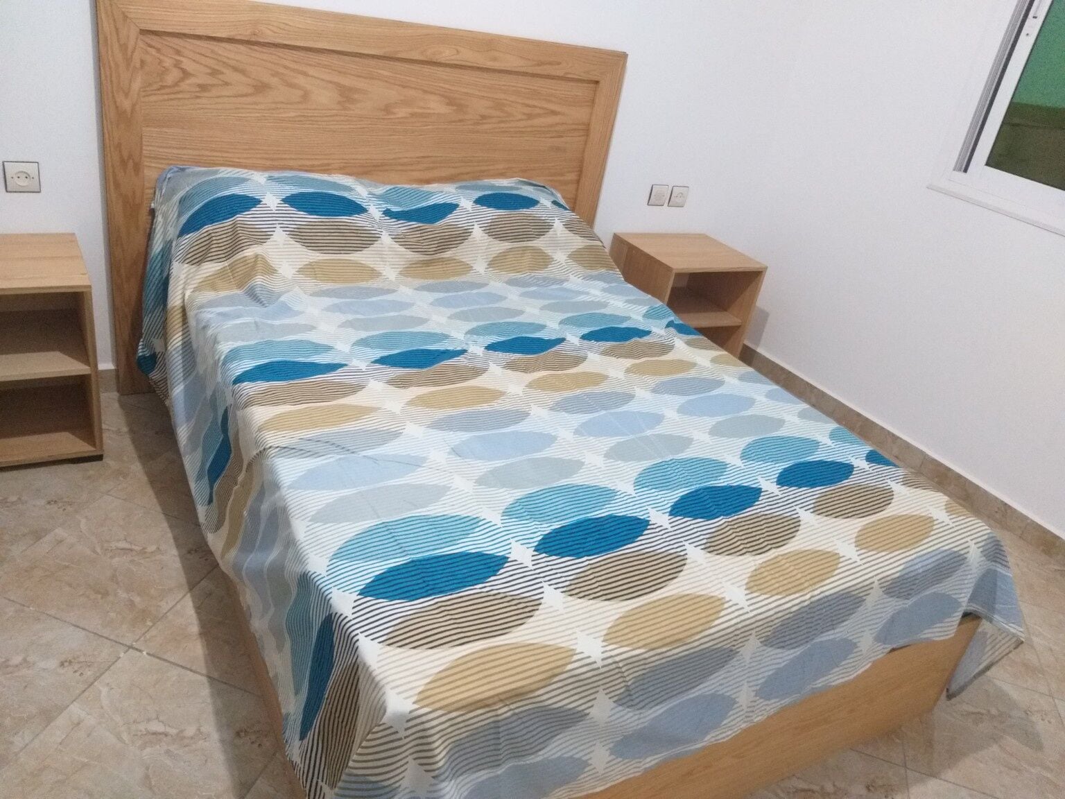 A single bed with a patterned bedspread, two bedside tables, and a window.