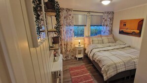 A bedroom with a bed, a bedside table with a lamp, a window with curtains, and a wall-mounted picture. - Room-cozy Room at Hilde & Tuti (Nærøysund)