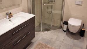 A modern bathroom with a glass-enclosed shower, a white sink with a dark cabinet, and a beige rug on the floor. - Room-cozy Room at Hilde & Tuti (Nærøysund)