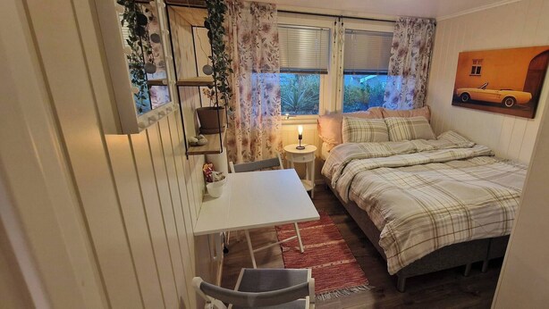 A compact bedroom with a bed, bedside table, and a small desk with a chair. - Room-cozy Room at Hilde & Tuti (Nærøysund)