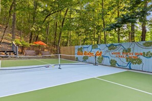Ein Tennisplatz im Freien mit Netz, umgeben von Holzfence und Bäumen.