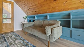 A room with a wooden ceiling, a sofa, a blue shelving unit, and a patterned rug. - Starry Skies: Sauna, S'mores & Pickleball Retreat (Blue Ridge)
