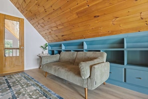 A room with a wooden ceiling, a sofa, a blue shelving unit, and a patterned rug. - Starry Skies: Sauna, S'mores & Pickleball Retreat (Blue Ridge)
