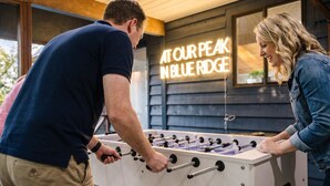 A foosball table in a room with a neon sign that reads 'AT OUR PEAK BLUE RIDGE'. - Starry Skies: Sauna, S'mores & Pickleball Retreat (Blue Ridge)