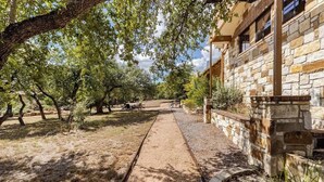 Un chemin mène à un bâtiment en pierre doté d’un espace extérieur abrité avec des sièges.