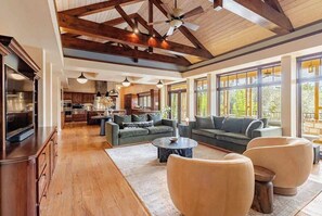 Ein großzügiges Wohnzimmer mit hoher Decke, großen Fenstern und einer modernen Küche im Hintergrund.